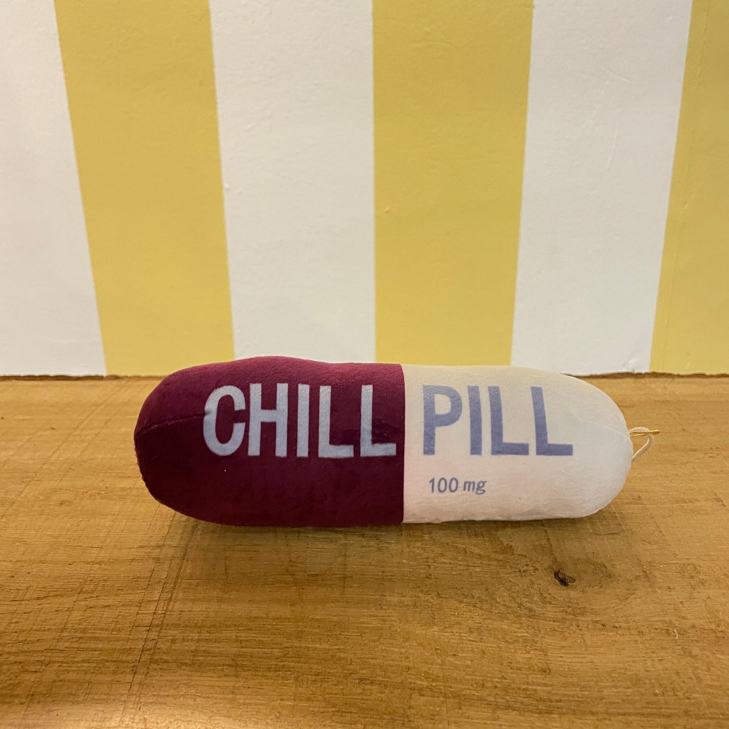 The Tetbury Pet Shop & Grooming's Chill Pill is a plush maroon and white capsule toy for dogs, labeled "CHILL PILL" and hanging from a clip—perfect as a quirky squeaky toy for your pup.