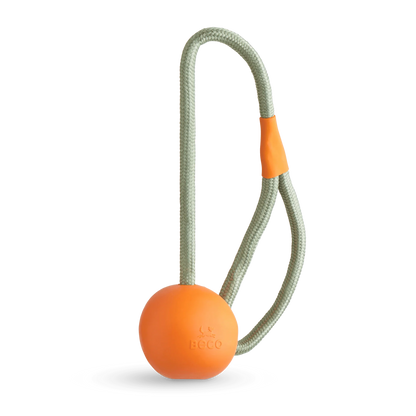 The Beco Slinger by The Tetbury Pet Shop & Grooming is an orange natural rubber fetch ball on a gray rope loop with an orange grip, designed for fun, interactive play with your dog.