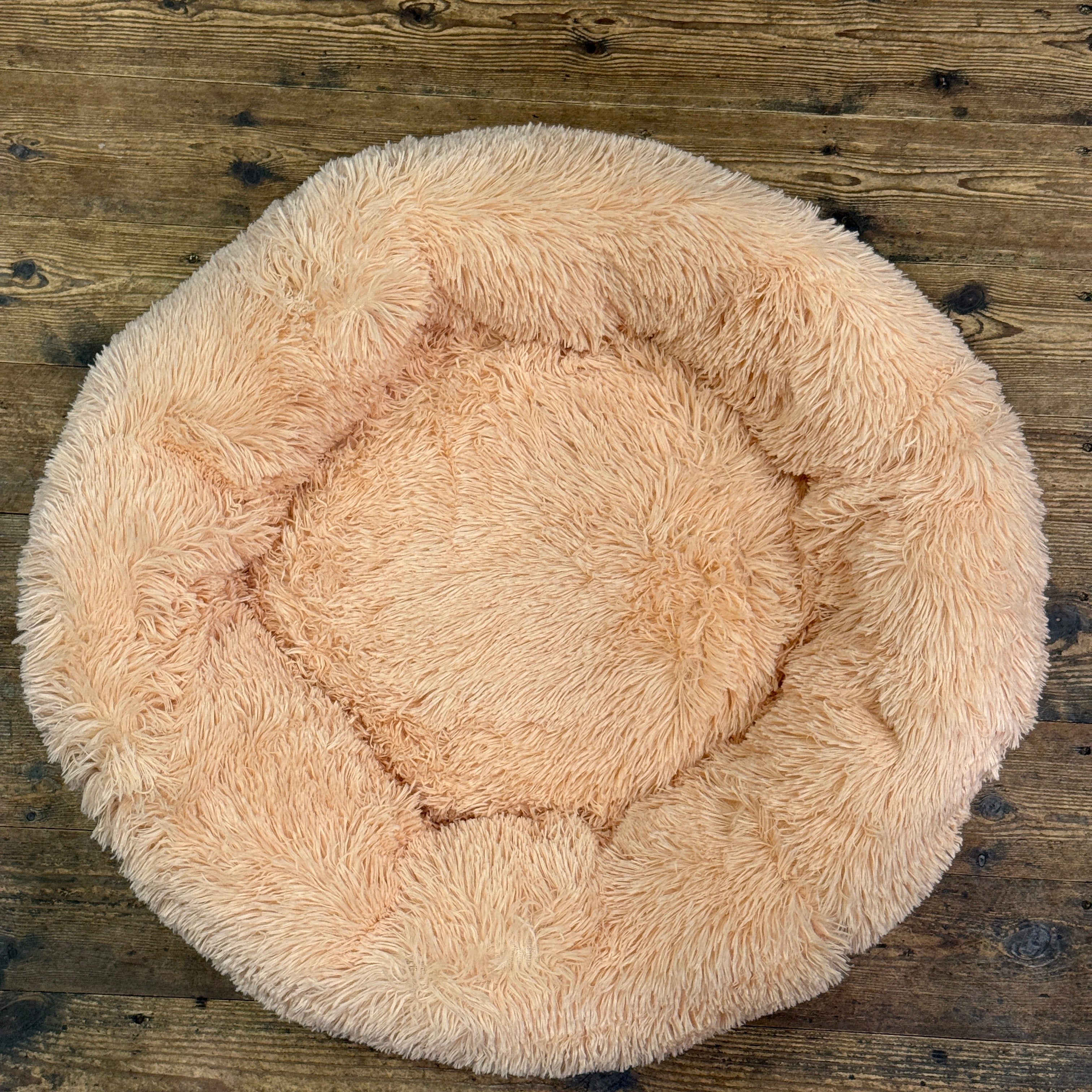 Round beige fluffy pet bed on a wooden floor