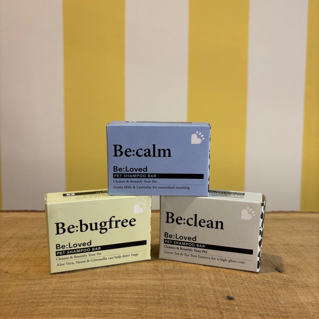 Three boxes of The Tetbury Pet Shop & Grooming's Be: Natural Shampoo Bars are stacked on wood with a yellow and white striped background, showcasing these eco-friendly pet shampoos.
