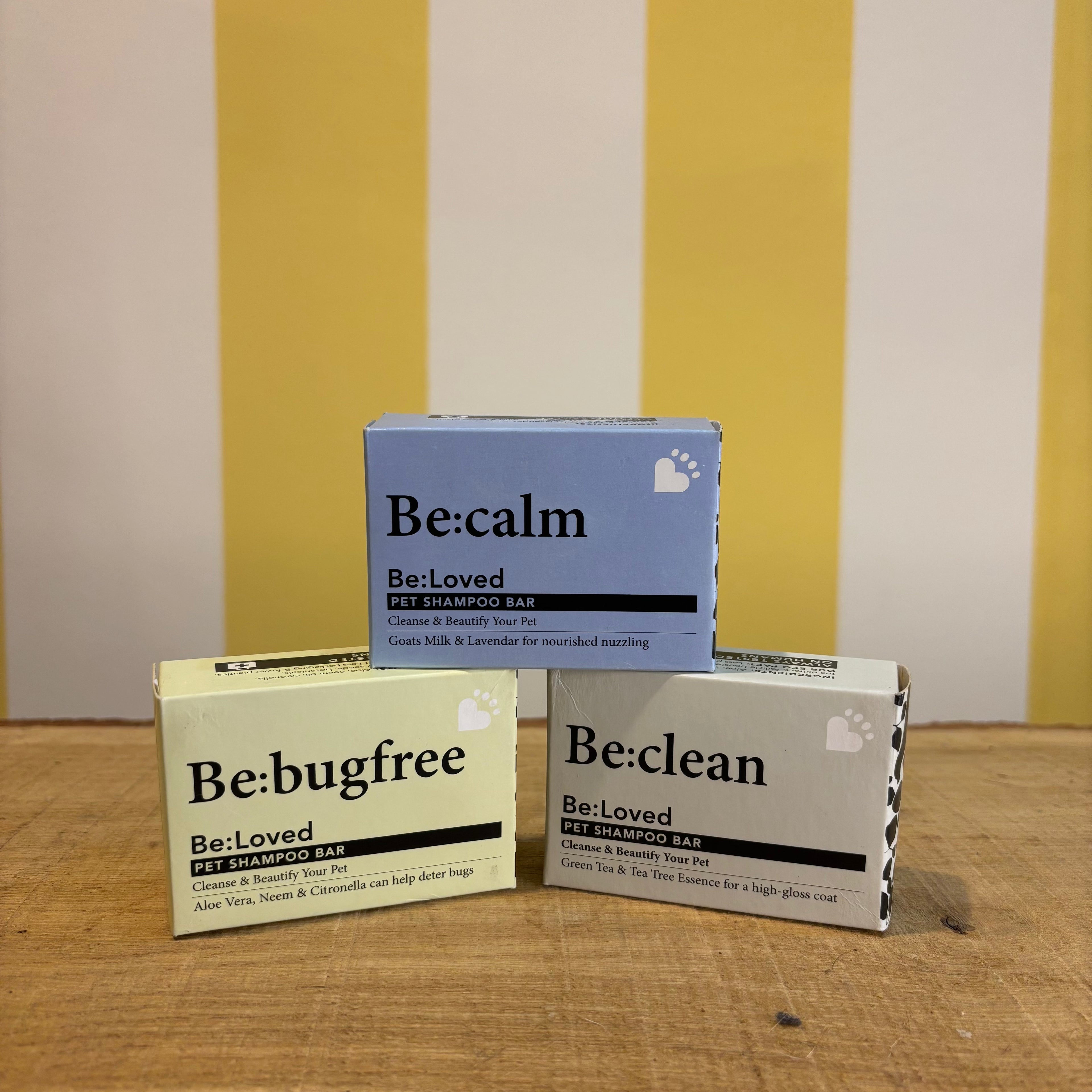 Three boxes of The Tetbury Pet Shop & Grooming's Be: Natural Shampoo Bars are stacked on wood with a yellow and white striped background, showcasing these eco-friendly pet shampoos.