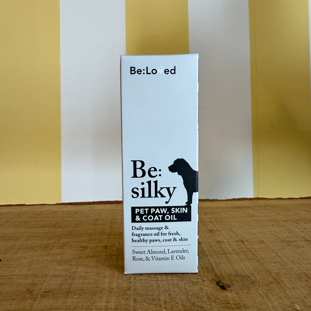 A brown glass dropper bottle and a box labeled Be:Silky Skin & Coat Oil Rub by The Tetbury Pet Shop & Grooming, both with dog silhouettes and ingredient lists, are set against a yellow and white background.