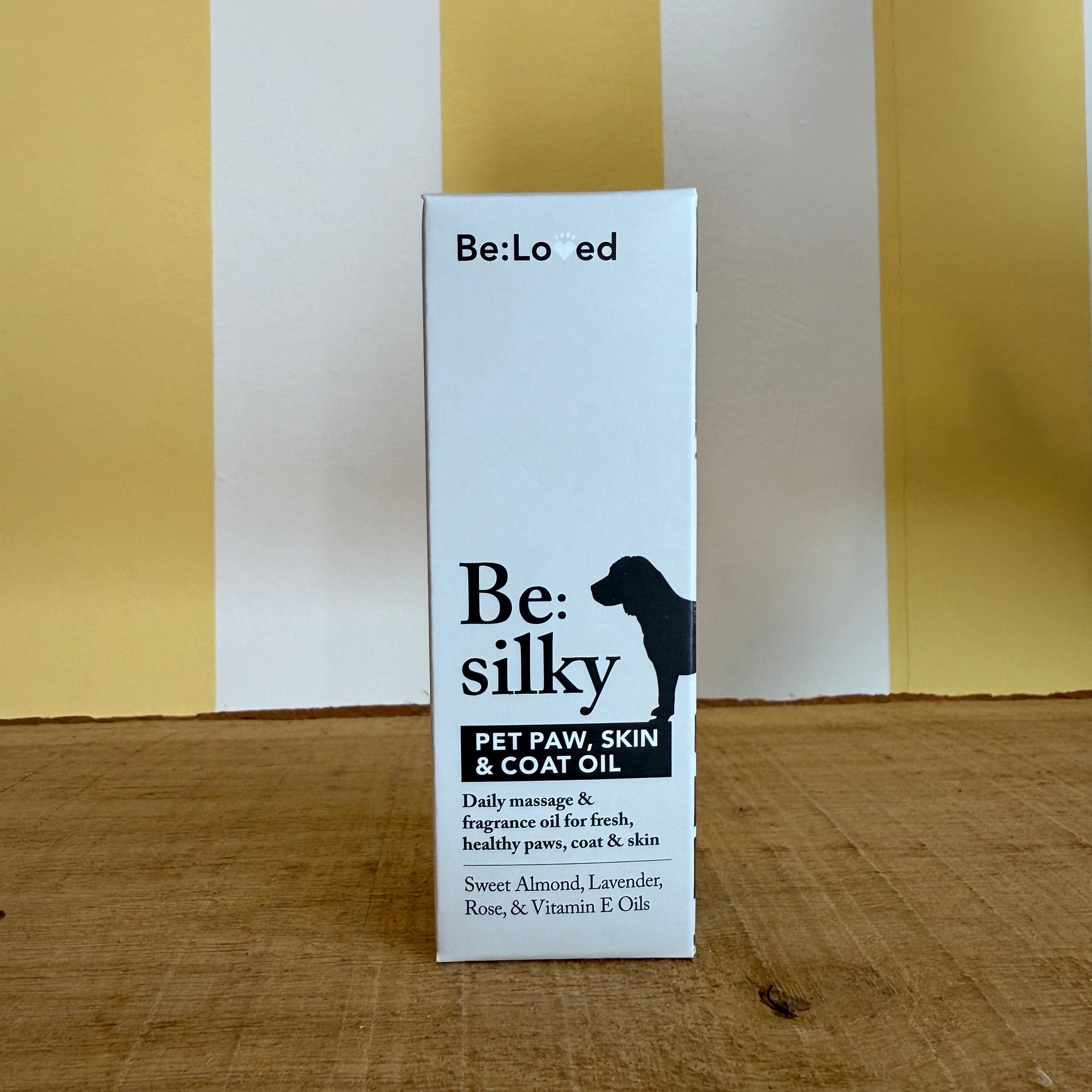 A brown glass dropper bottle and a box labeled Be:Silky Skin & Coat Oil Rub by The Tetbury Pet Shop & Grooming, both with dog silhouettes and ingredient lists, are set against a yellow and white background.