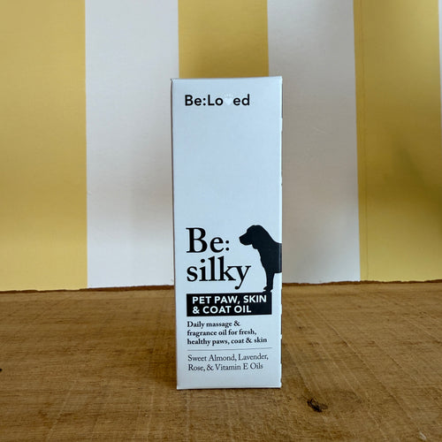 A brown glass dropper bottle and a box labeled Be:Silky Skin & Coat Oil Rub by The Tetbury Pet Shop & Grooming, both with dog silhouettes and ingredient lists, are set against a yellow and white background.