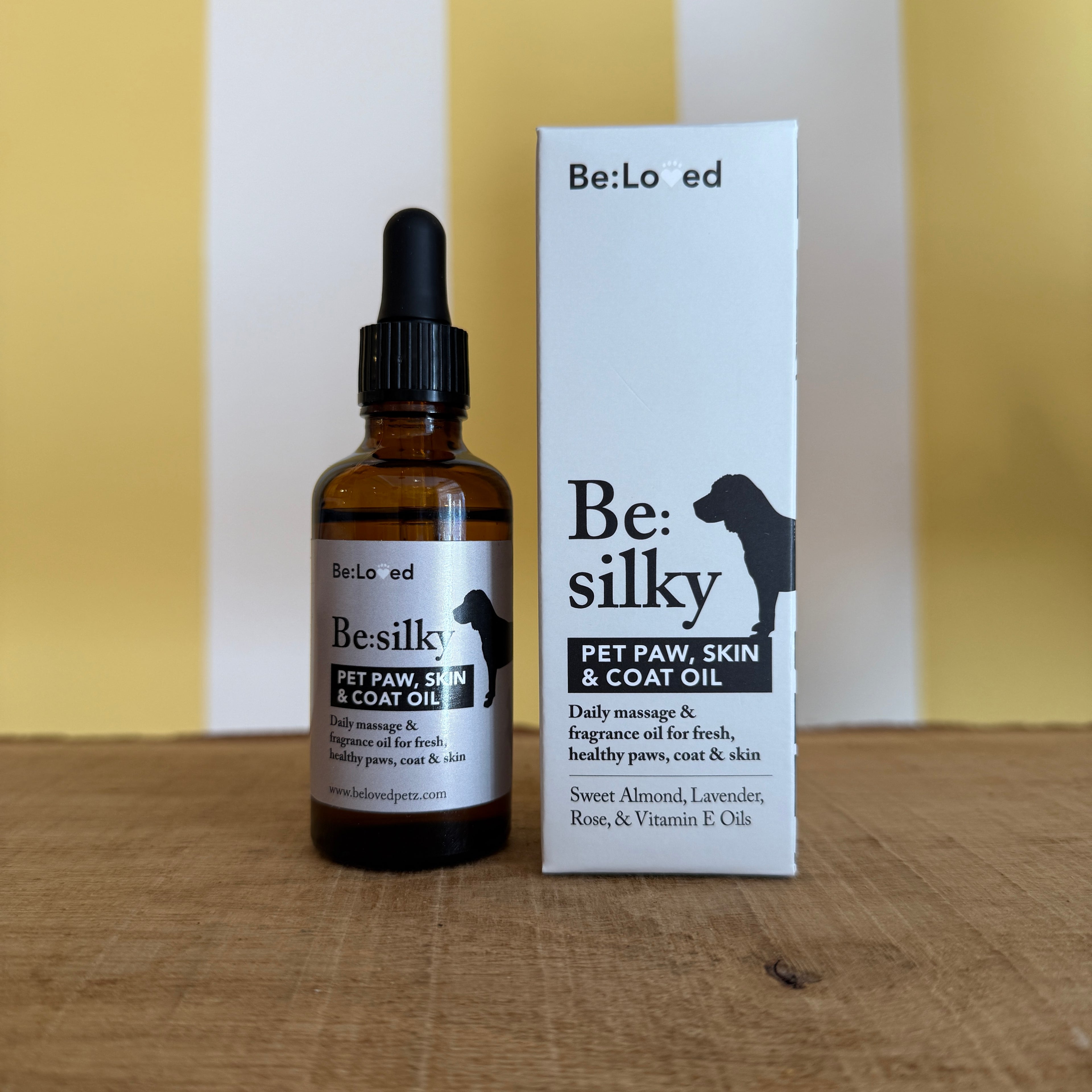 A brown glass dropper bottle and a box labeled Be:Silky Skin & Coat Oil Rub by The Tetbury Pet Shop & Grooming, both with dog silhouettes and ingredient lists, are set against a yellow and white background.