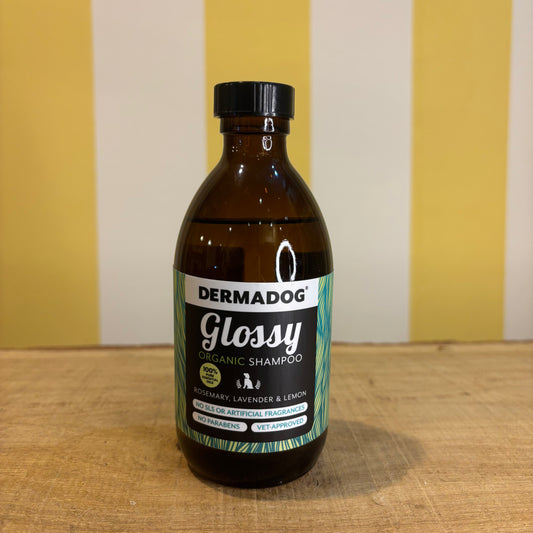 A brown bottle of Dermadog Shampoo rests on wood with a yellow and white striped background—an ideal pick for natural dog grooming.