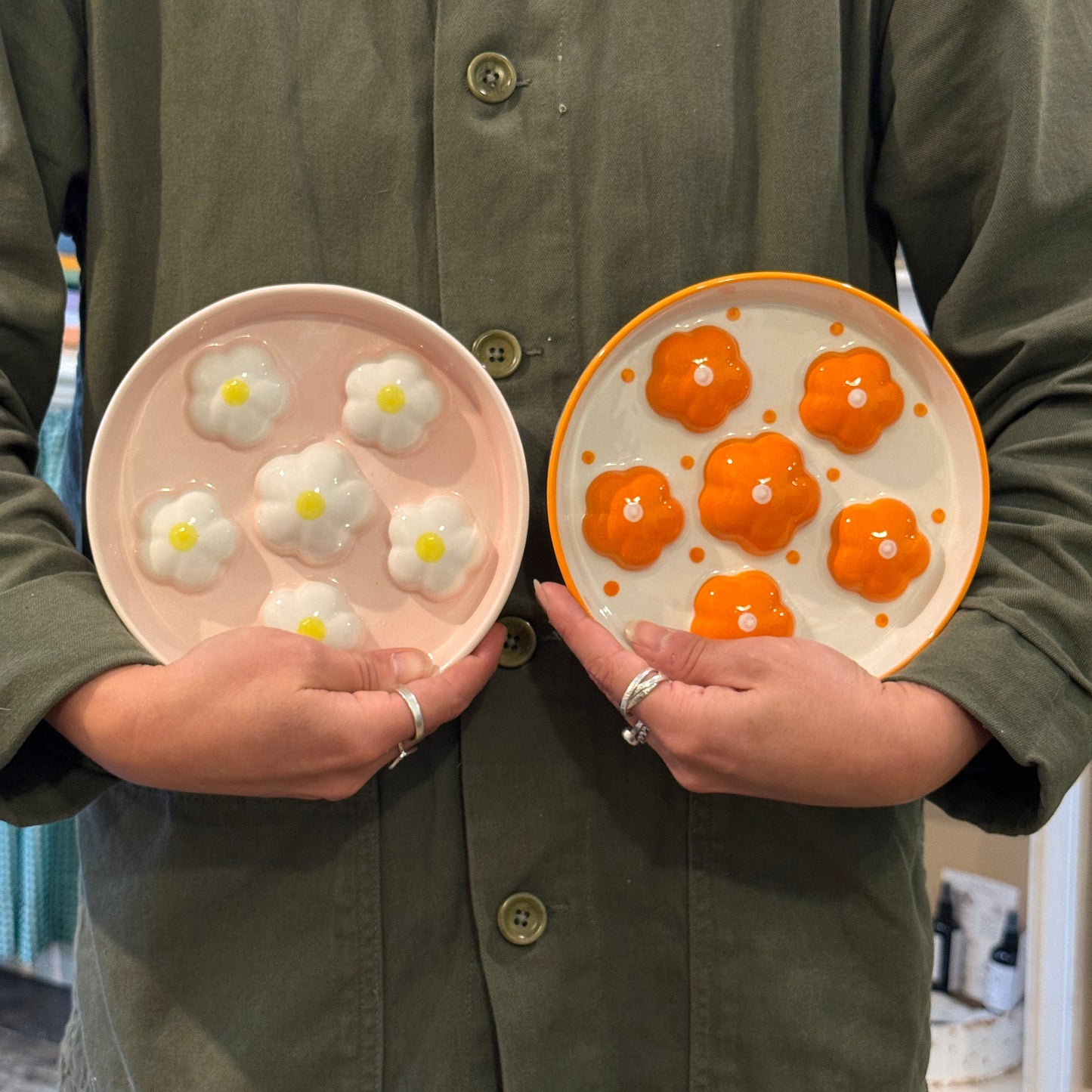 Two plates with floral designs held by a person wearing a green jacket.