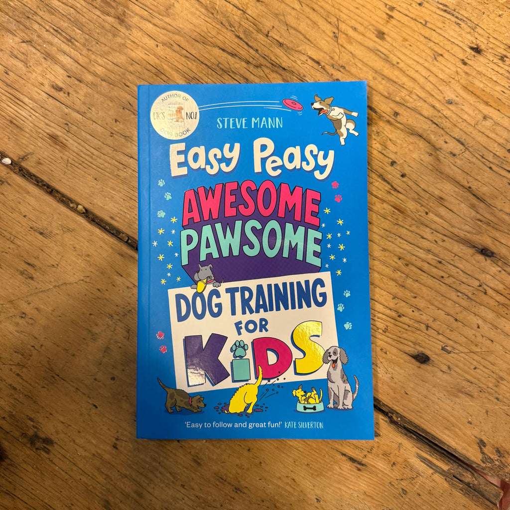 A blue copy of "Easy Peasy Awesome Pawsome Dog Training For Kids" by The Tetbury Pet Shop & Grooming lies on a wooden floor, its cover displaying colorful text and cartoon dogs to make training fun for kids.