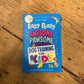 A blue copy of "Easy Peasy Awesome Pawsome Dog Training For Kids" by The Tetbury Pet Shop & Grooming lies on a wooden floor, its cover displaying colorful text and cartoon dogs to make training fun for kids.