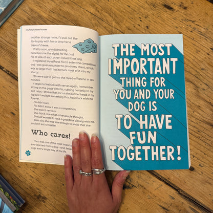 A blue copy of "Easy Peasy Awesome Pawsome Dog Training For Kids" by The Tetbury Pet Shop & Grooming lies on a wooden floor, its cover displaying colorful text and cartoon dogs to make training fun for kids.