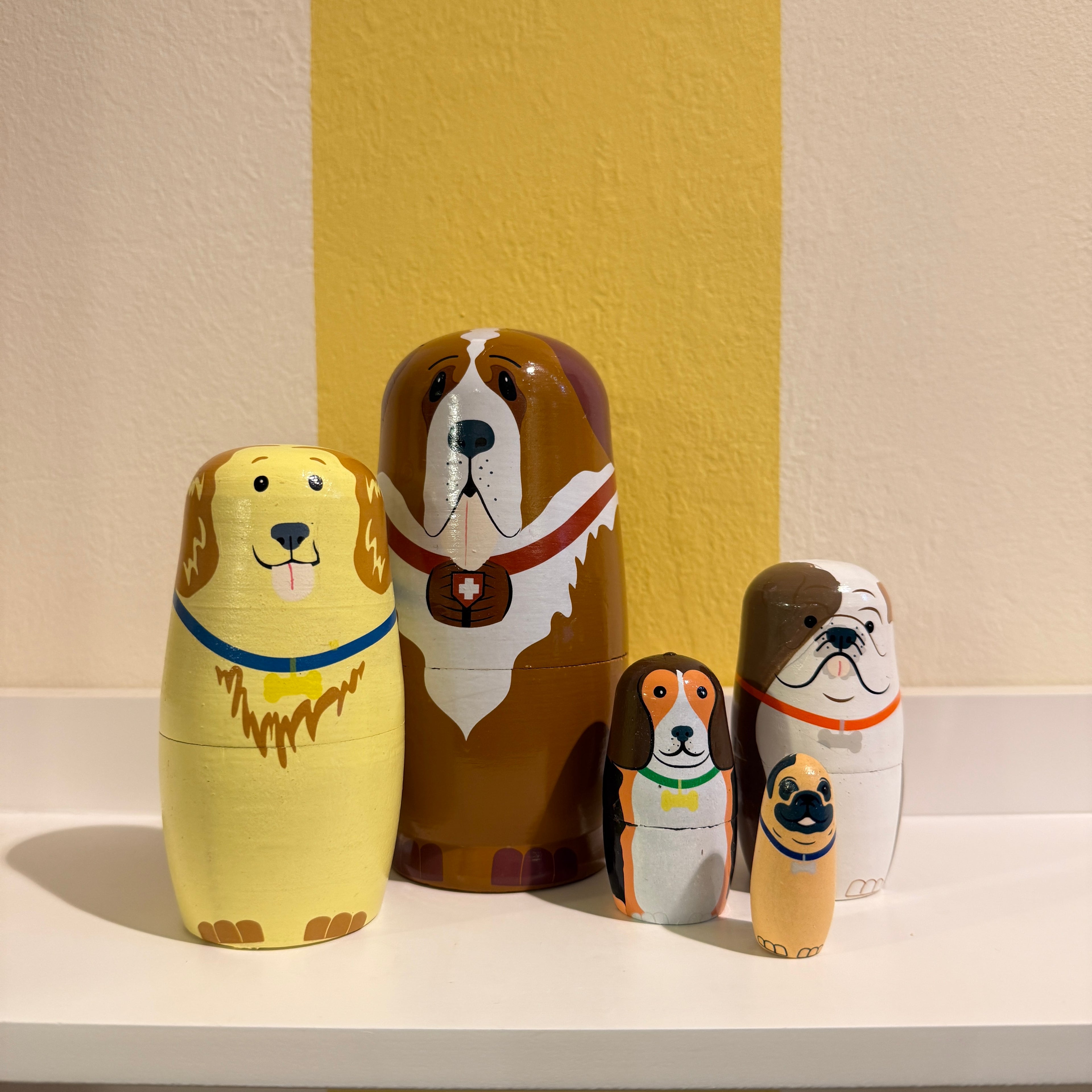 Set of wooden nesting dolls shaped like dogs on a white surface with a yellow wall background.